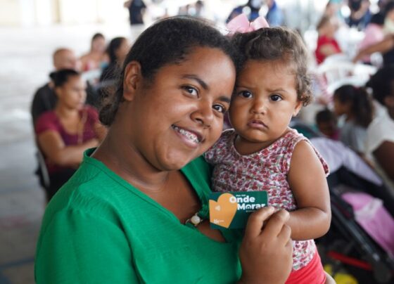 Beneficiária com bebê no colo segurando cartão do Aluguel Social