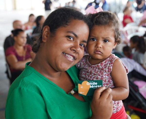 Beneficiária com bebê no colo segurando cartão do Aluguel Social