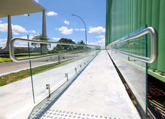 Imagem colorida horizontal de uma rampa com um corrimão cinza e proteção de vidro. Ao fundo o edifício-sede do STF e o céu azul