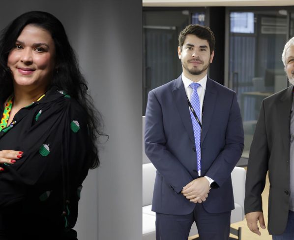 Foto colorida em formato horizontal. Á esquerda aparece uma mulher branca de cabelos pretos e cacheado, com o braço cruzado, roupas pretas e o cordão colorido com símbolos de quebra cabeça e a direita um homem adulto jovem com cabelos pretos e terno azul, e ao lado dele um homem com cabelos grisalhos e barba, usando blusa cinza, blaser preto e calça preta