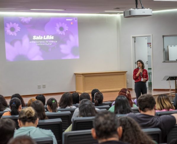O Hospital Estadual de Urgências Governador Otávio Lage de Siqueira (Hugol) inaugurou, nesta quinta-feira (28/05), sua Sala Lilás, espaço destinado ao acolhimento e apoio de mulheres vítimas de violência. A iniciativa tem como objetivo fortalecer a assistência humanizada e garantir um atendimento mais seguro, reservado e acolhedor às vítimas atendidas. A Sala Lilás foi estruturada para oferecer privacidade, escuta qualificada e suporte durante o atendimento multiprofissional. O ambiente também poderá ser utilizado em atendimentos que que também envolvam crianças e adolescentes em situação de vulnerabilidade. O evento reuniu 168 profissionais do hospital, entre equipes assistenciais, multiprofissionais e setores estratégicos, reforçando a importância da qualificação contínua para o atendimento humanizado e identificação precoce de situações de violência. A inauguração contou com palestra voltada aos profissionais, ministrada pela coordenadora-geral dos Ciclos de Vida e Violências na Superintendência de Políticas e Atenção Integral à Saúde da Secretaria da Saúde de Goiás, Lígia da Fonseca Bernardes. Ela abordou temas relacionados ao enfrentamento da violência contra a mulher, incluindo: fluxo de atendimento dos casos; violência de gênero; Lei Maria da Penha; tipos de violência; ciclo da violência; identificação de sinais de abuso e vulnerabilidade. Capacitção das equipes Segundo Lígia, a capacitação das equipes de saúde é fundamental para garantir acolhimento adequado às vítimas. “Os profissionais da saúde têm papel essencial na identificação precoce dos sinais de violência e no acolhimento humanizado dessas mulheres”. “Muitas vezes, o hospital é a primeira porta de apoio procurada pela vítima, e estar preparado para esse atendimento pode fazer toda a diferença no rompimento do ciclo da violência”, destacou. Sala Lilás – avanço no cuidado De acordo com a supervisora multiprofissional do Hugol, Gabriela Vieira, a implantação da Sala Lilás representa um avanço importante no cuidado às vítimas em situação de vulnerabilidade. “A criação desse espaço fortalece o acolhimento humanizado dentro da unidade e proporciona mais segurança, privacidade e suporte emocional às pacientes atendidas. É um ambiente pensado para oferecer escuta qualificada e assistência integral”, afirmou. A criação da Sala Lilás integra as ações de fortalecimento das políticas de proteção e cuidado às vítimas de violência desenvolvidas pelo Hugol, promovendo um ambiente mais acolhedor e preparado para assistência integral aos pacientes em situação de vulnerabilidade. Além do acolhimento imediato, o espaço também busca contribuir para o encaminhamento adequado das vítimas à rede de apoio e proteção, fortalecendo o trabalho integrado entre saúde, assistência social e segurança pública. Saiba mais Sala Lilás do Hugol vai acolher mulheres vítimas de violência
