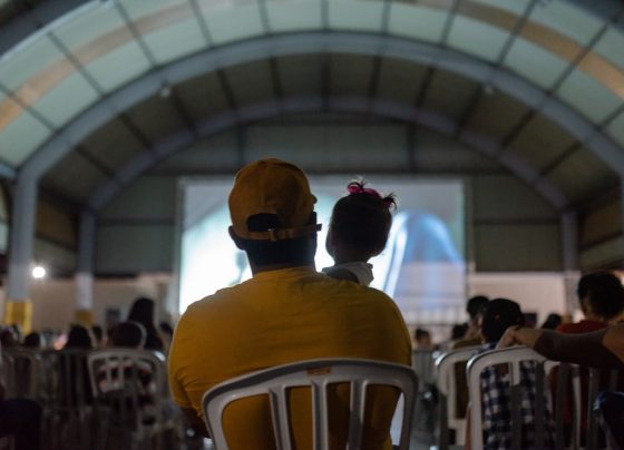 Governo de Goiás leva Cine Leitura do Bem a mais quatro municípios - público assistindo a sessão de cinema do projeto. Em primeiro plano, pai com bebê nos braços assistindo ao filme