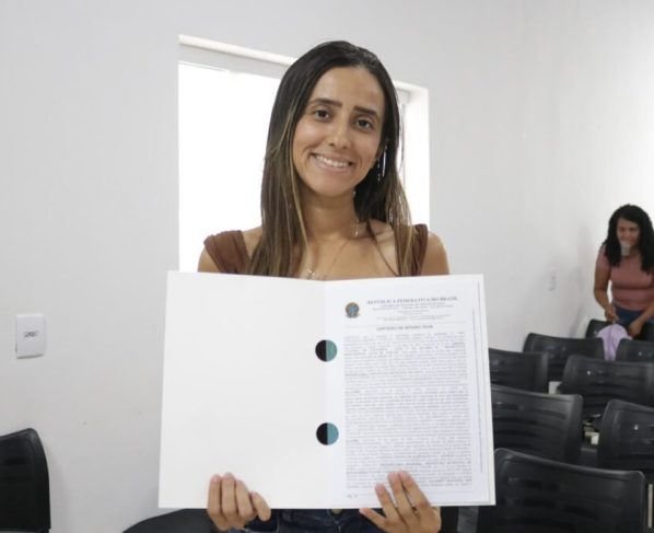Governo de Goiás entrega 98 escrituras de casas a custo zero em Bom Jardim e Piranhas - Mulher jovem e de cabelos longos com escritura em mãos