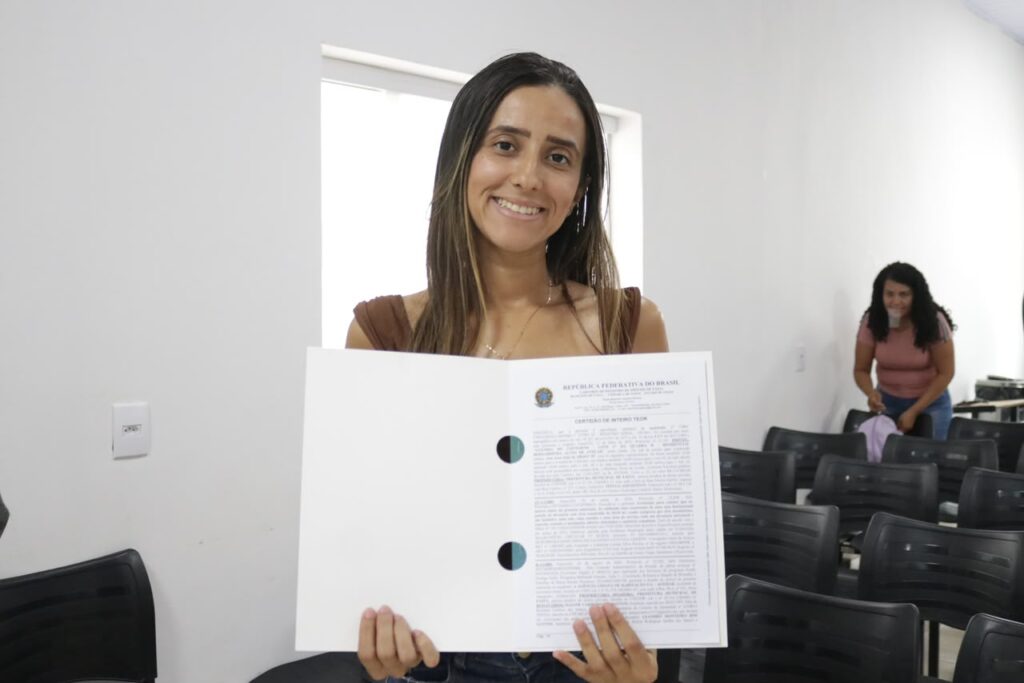 Governo de Goiás entrega 98 escrituras de casas a custo zero em Bom Jardim e Piranhas - Mulher jovem e de cabelos longos com escritura em mãos